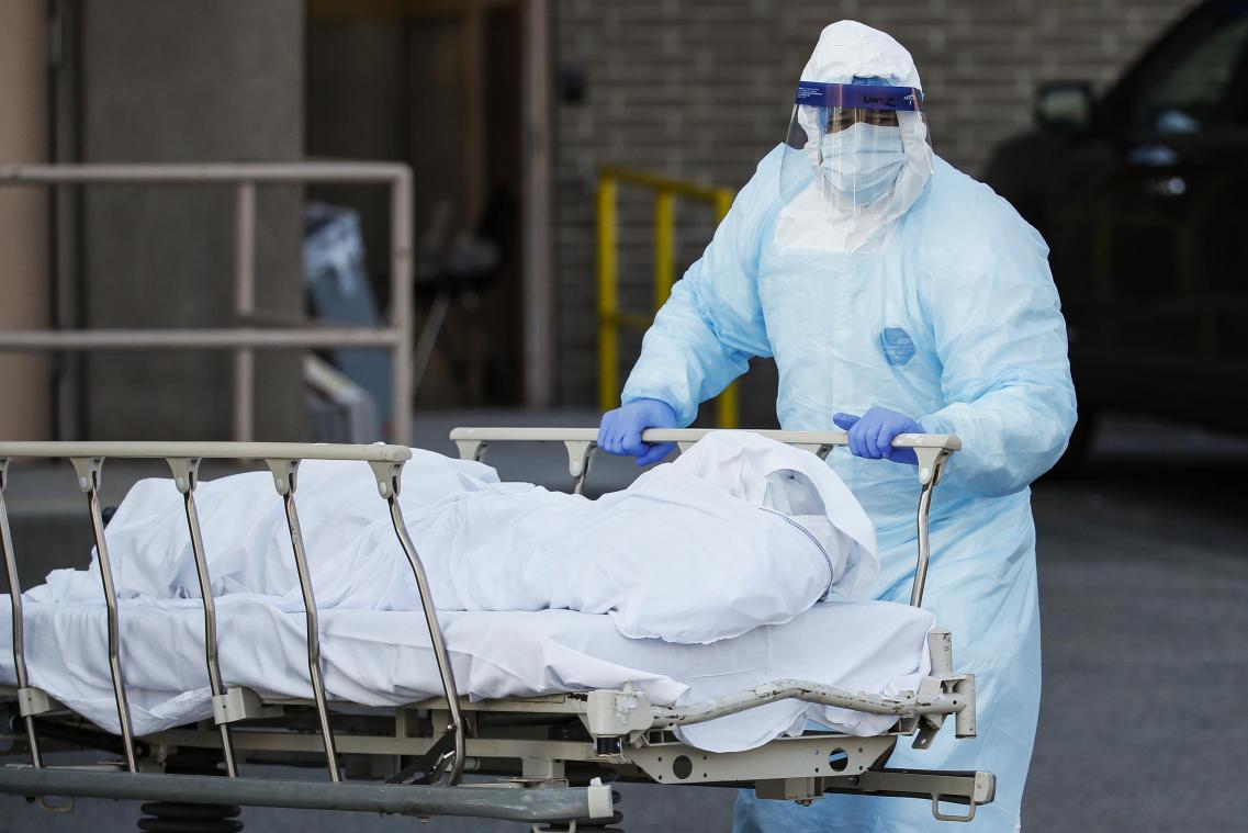 <p>Ein medizinischer Mitarbeiter in Schutzkleidung rollt eine Leiche zu einem Kühlanhänger, der als behelfsmäßige Leichenhalle im Wyckoff Heights Medical Center dient.</p>