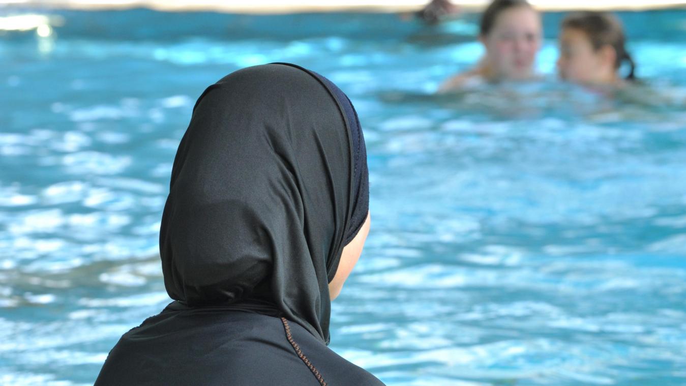 <p>Eine muslimische Schülerin sitzt in einem Ganzkörperbadeanzug (Burkini) am Rande eines Schwimmbeckens.</p>