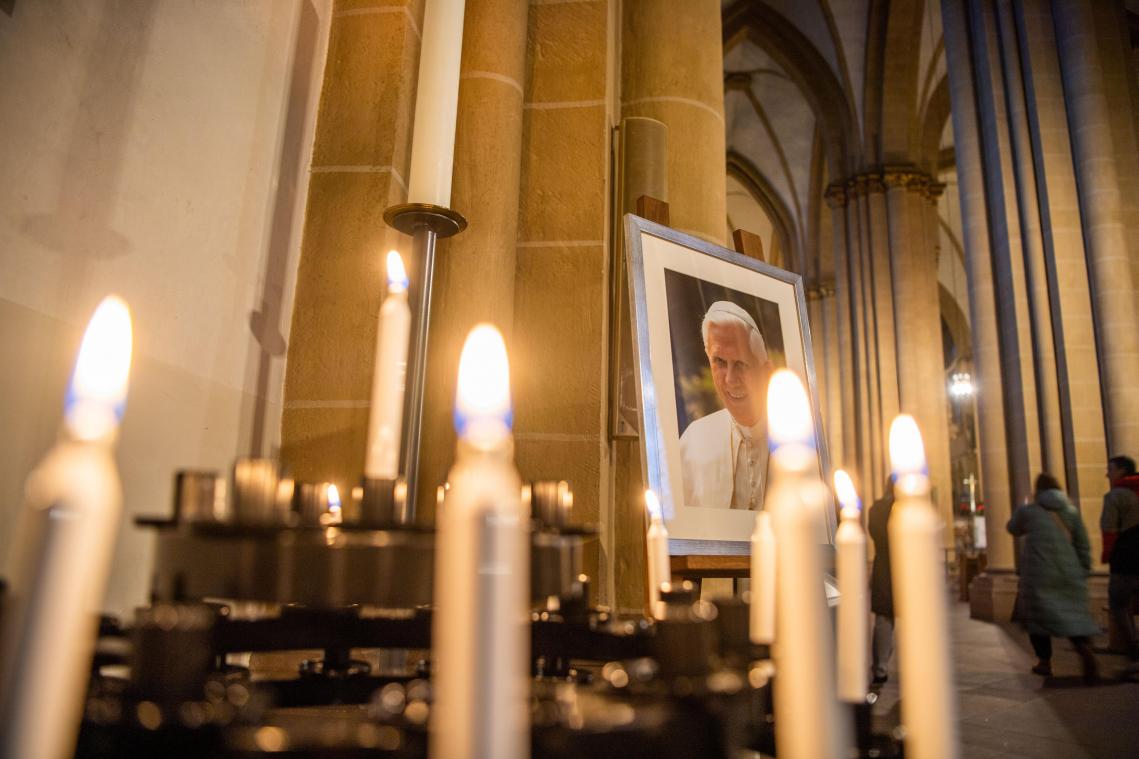 <p>Ein Porträtbild vom emeritierten Papst Benedikt XVI. steht hinter Andachtskerzen im Paderborner Dom.</p>