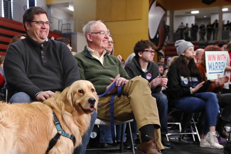 <p>Sohn Alex Warren (l.) und Warrens Ehemann Bruce Mann sitzen mit Familienhund Bailey im Publikum, während die demokratische Präsidentschaftskandidatin Elizabeth Warren bei einer Wahlkampfveranstaltung in Cedar Rapids spricht.</p>